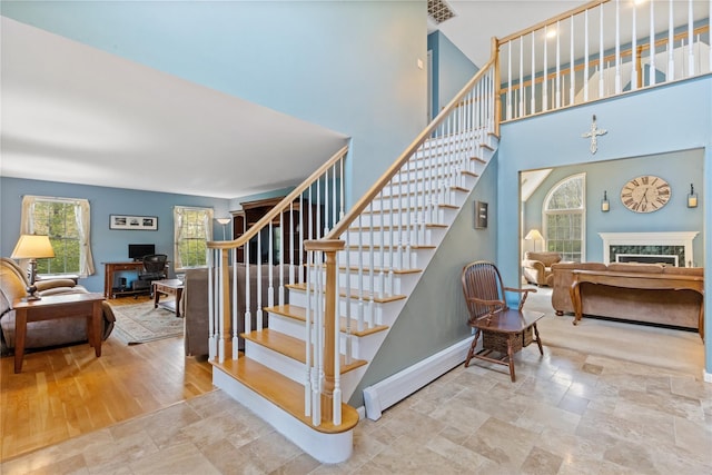 stairs featuring baseboards, stone finish floor, a high ceiling, and a fireplace