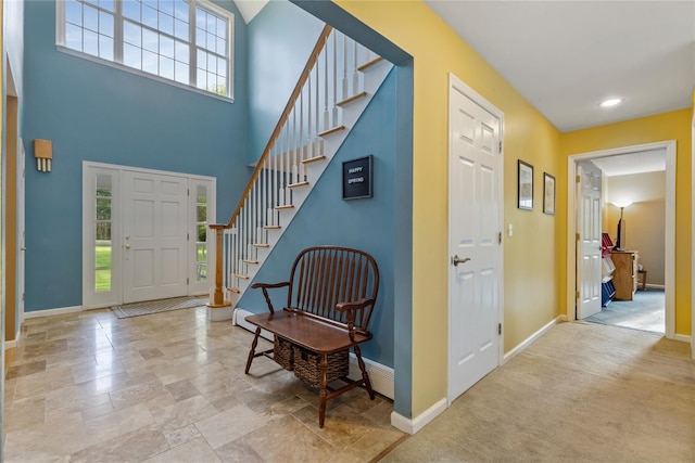 entryway with baseboards, stone finish flooring, stairs, and a towering ceiling