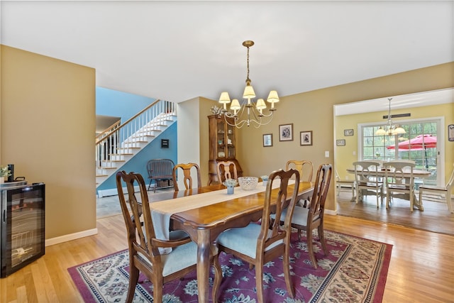 dining room featuring stairs, an inviting chandelier, light wood-type flooring, and wine cooler