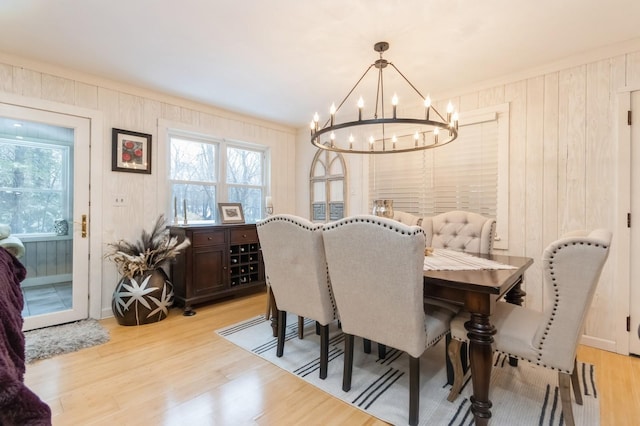 dining area with a chandelier, plenty of natural light, light wood-style flooring, wood walls, and crown molding