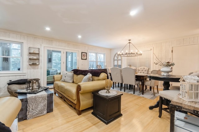 living area with a chandelier, light wood-type flooring, wooden walls, and ornamental molding
