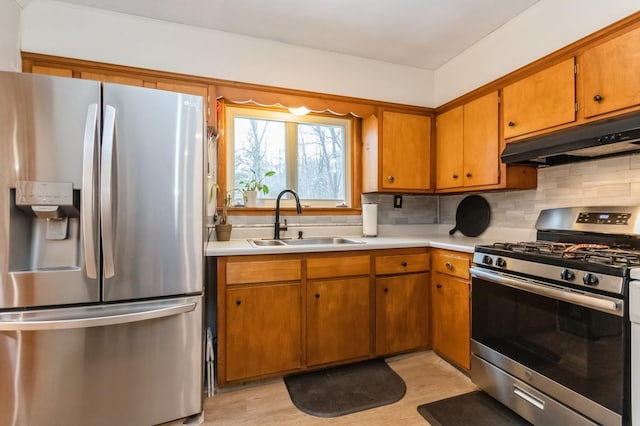 kitchen with appliances with stainless steel finishes, under cabinet range hood, a sink, light countertops, and backsplash