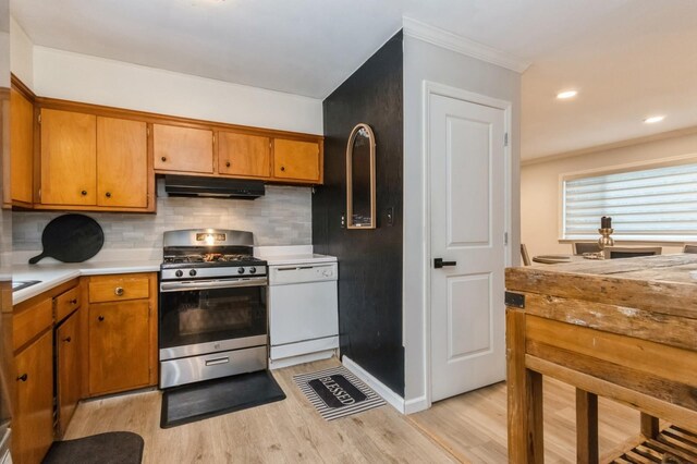 kitchen with gas stove, white dishwasher, under cabinet range hood, light wood-style floors, and crown molding