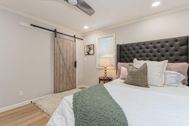 bedroom with a barn door, wood finished floors, crown molding, baseboards, and ceiling fan
