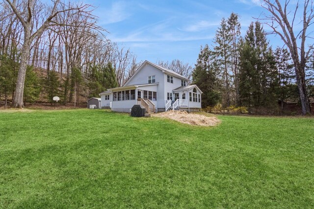 back of house with a sunroom, a storage unit, a lawn, and an outdoor structure