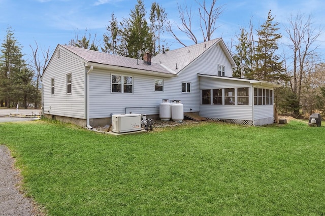 back of house with a sunroom, a lawn, a chimney, and roof with shingles