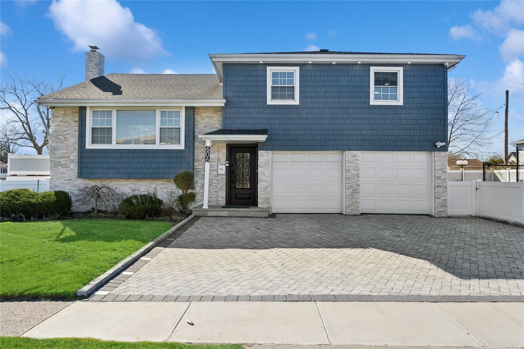 606 Flanders Dr, North Woodmere, NY 11581 - split level home featuring fence, stone siding, driveway, a front yard, and a chimney