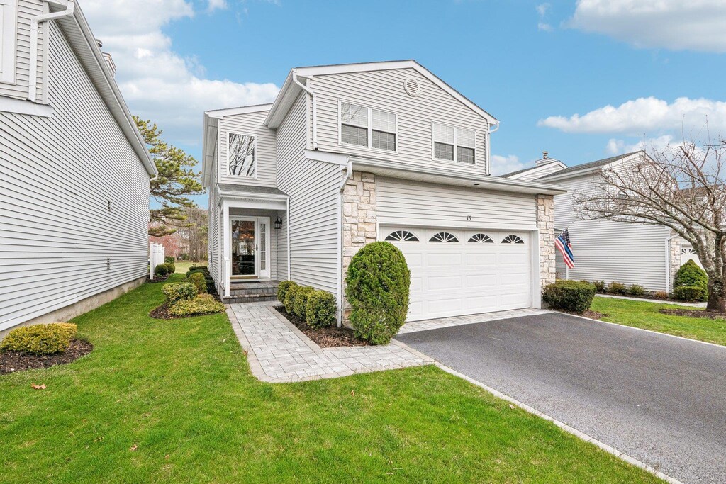 traditional-style house featuring a front lawn, stone siding, a garage, and aphalt driveway