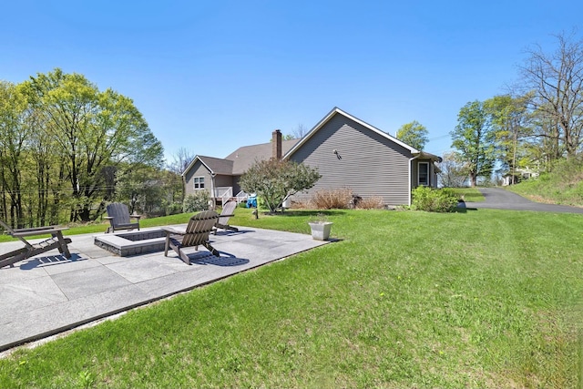 rear view of house featuring a lawn, a patio area, a fire pit, and a chimney
