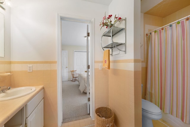 ensuite bathroom with tile walls, wainscoting, curtained shower, vanity, and toilet