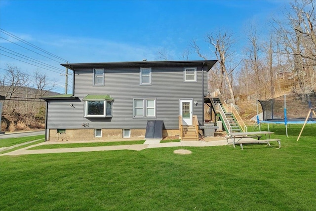 back of house with stairway, a yard, and a trampoline