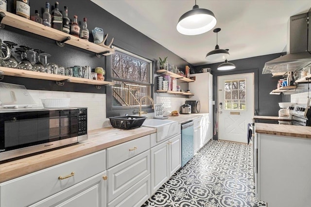 kitchen with wall chimney range hood, open shelves, a sink, wood counters, and stainless steel appliances