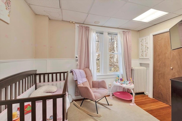 bedroom with wainscoting, a paneled ceiling, wood finished floors, and radiator