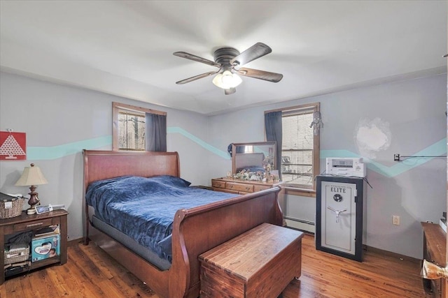 bedroom with a baseboard heating unit, wood finished floors, and ceiling fan