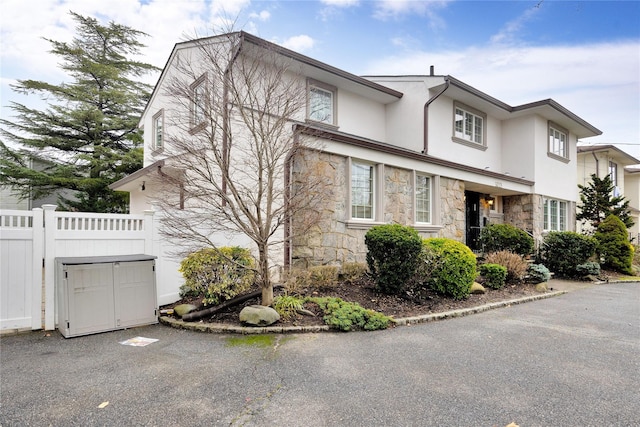 view of front of house featuring stucco siding, stone siding, and fence