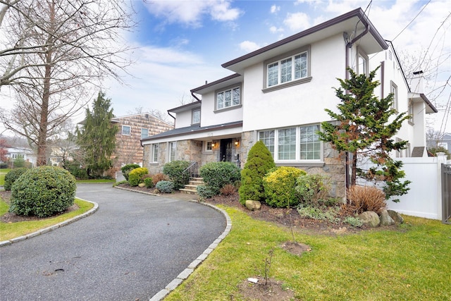 view of front facade with fence, stucco siding, a front lawn, and stone siding