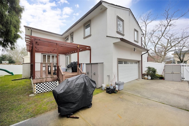 rear view of property with a wooden deck, fence, stucco siding, a gate, and concrete driveway