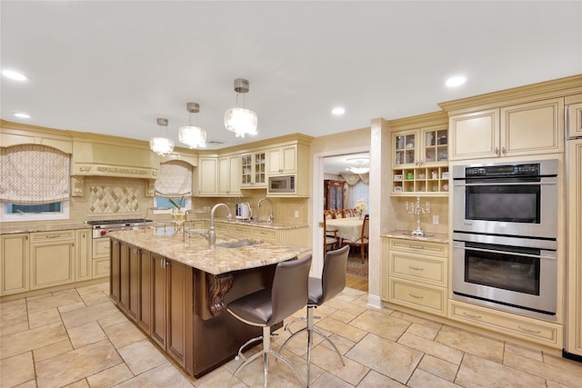 kitchen featuring tasteful backsplash, a sink, light stone counters, stainless steel appliances, and cream cabinetry