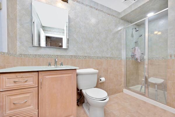bathroom with vanity, toilet, tile walls, tile patterned floors, and a stall shower
