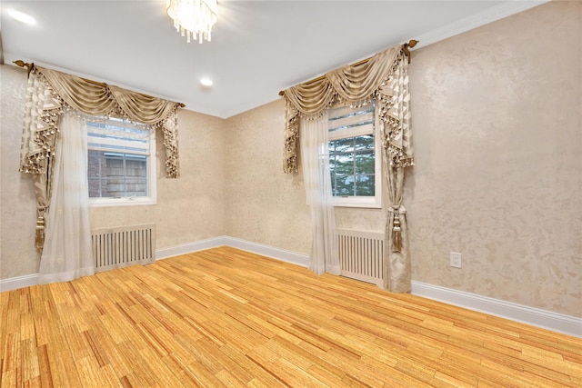 unfurnished room with ornamental molding, a notable chandelier, wood finished floors, and radiator heating unit