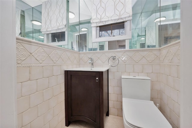 bathroom featuring toilet, tile patterned floors, tile walls, and vanity