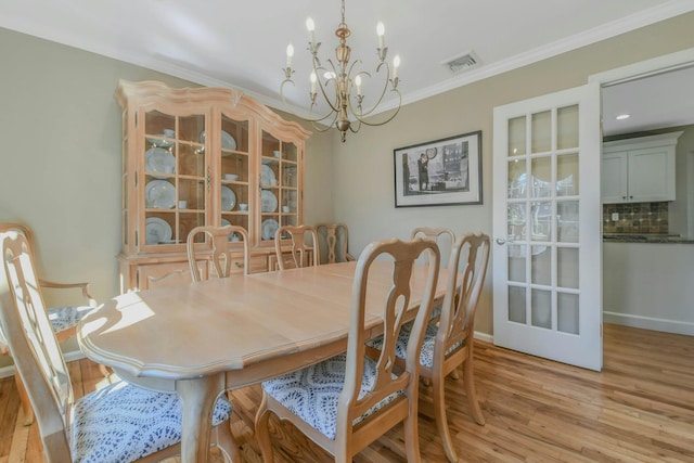 dining area with crown molding, baseboards, a chandelier, visible vents, and light wood-style flooring