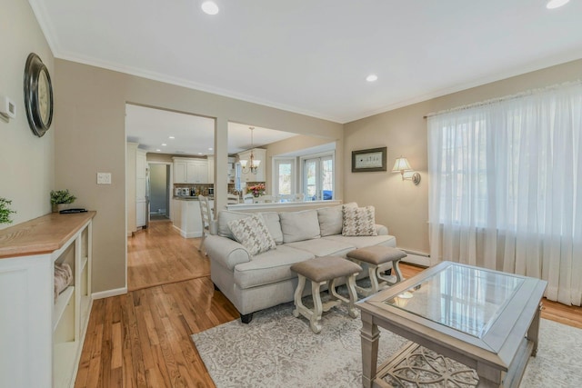 living room featuring a chandelier, light wood finished floors, baseboards, a baseboard heating unit, and ornamental molding