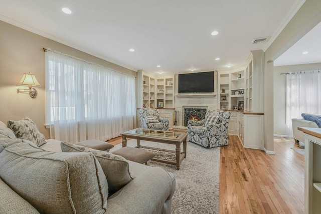 living room featuring light wood-style flooring, crown molding, a lit fireplace, and visible vents