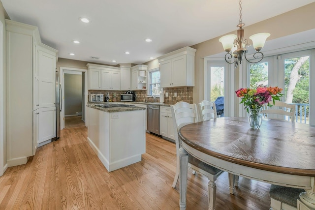 kitchen featuring an inviting chandelier, appliances with stainless steel finishes, light wood finished floors, and decorative backsplash