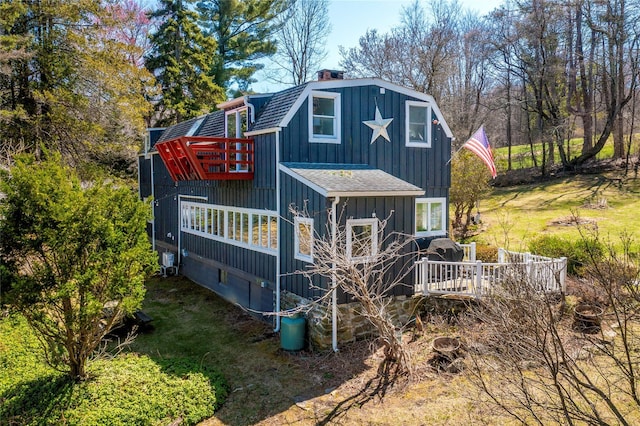 back of property with board and batten siding, a chimney, roof with shingles, a deck, and a gambrel roof