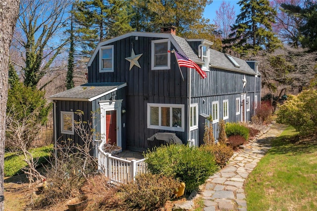 view of front of home featuring board and batten siding, a chimney, roof with shingles, and a gambrel roof