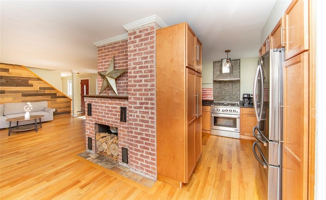 kitchen with a brick fireplace, dark countertops, light wood-style floors, wall chimney exhaust hood, and appliances with stainless steel finishes