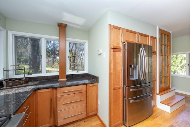 kitchen featuring dark stone counters, stainless steel refrigerator with ice dispenser, brown cabinets, and light wood-style flooring