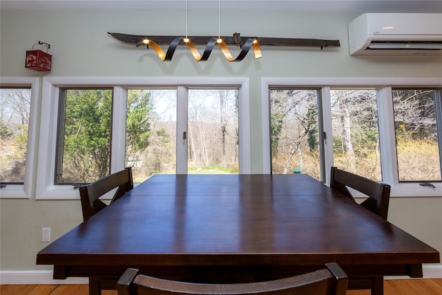dining room with an AC wall unit, baseboards, plenty of natural light, and wood finished floors