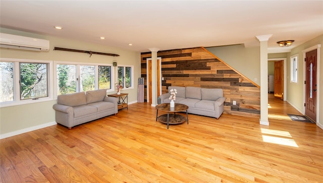 living room with an AC wall unit, decorative columns, and light wood-style flooring
