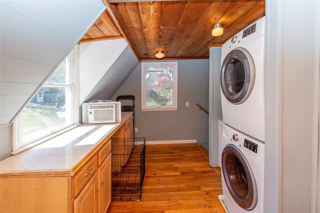 clothes washing area featuring laundry area, light wood-style flooring, baseboards, wooden ceiling, and stacked washer / dryer