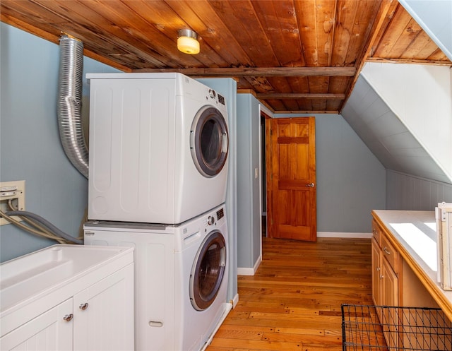 clothes washing area featuring wood ceiling, light wood-type flooring, cabinet space, stacked washing maching and dryer, and baseboards