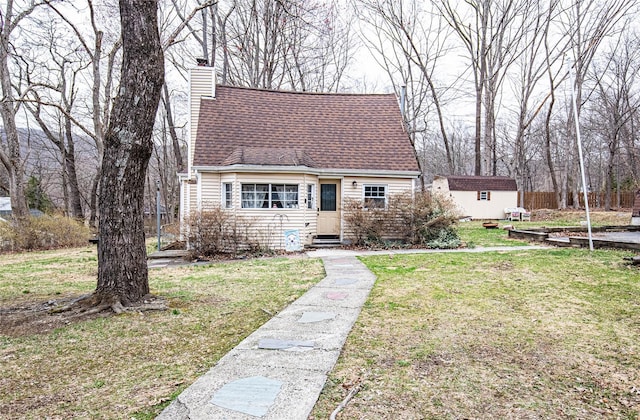 view of front of property with an outbuilding, roof with shingles, a storage shed, a front lawn, and a chimney