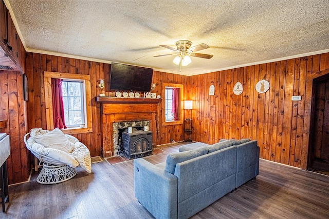 living area with a textured ceiling, wood finished floors, a wood stove, and a ceiling fan