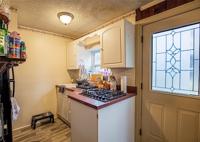 kitchen with light wood finished floors, white cabinetry, black gas stovetop, and a textured ceiling