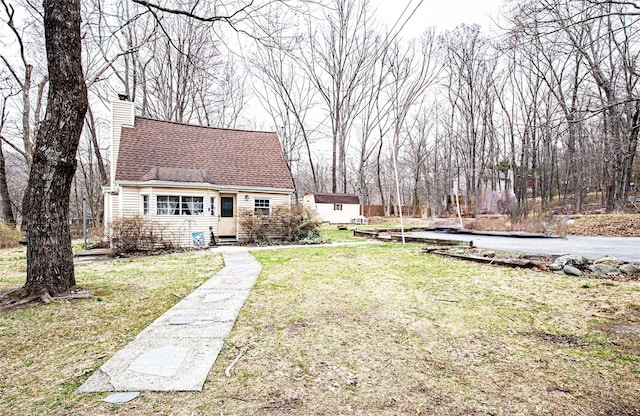 view of front of property with a chimney, a front lawn, an outdoor structure, and roof with shingles