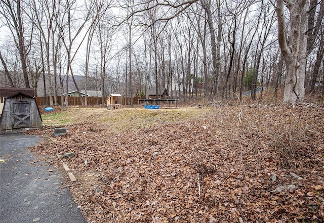 view of yard featuring a storage unit, fence, an outdoor structure, and a trampoline