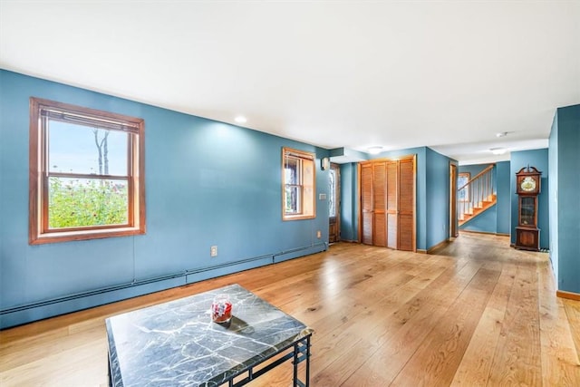 living room with baseboards, stairs, light wood-type flooring, and a baseboard radiator