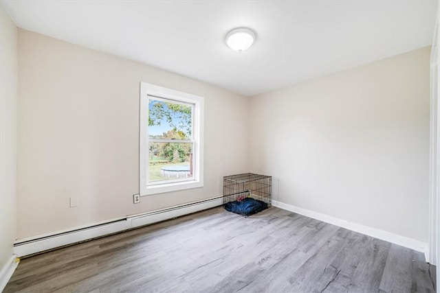spare room with baseboards, wood finished floors, and a baseboard heating unit