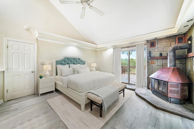 bedroom with high vaulted ceiling, wood finished floors, a ceiling fan, access to exterior, and a wood stove