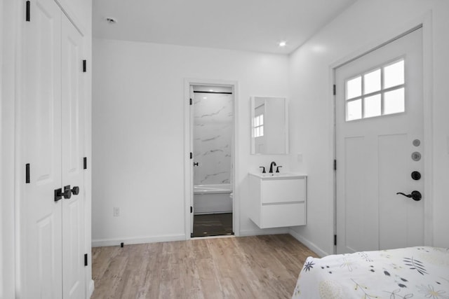 bedroom featuring ensuite bathroom, baseboards, a sink, and light wood-style floors