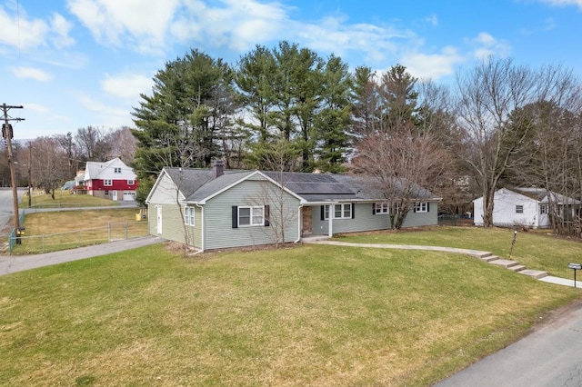 single story home featuring a chimney, fence, solar panels, driveway, and a front yard