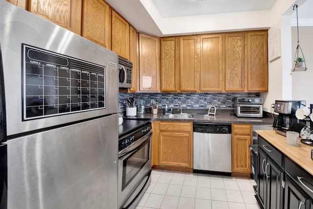 kitchen featuring dark countertops, tasteful backsplash, a sink, stainless steel appliances, and light tile patterned flooring