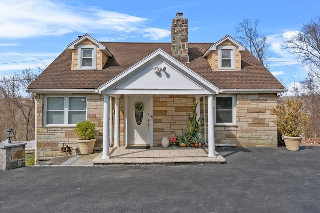 view of front of home with a chimney, a shingled roof, and stone siding