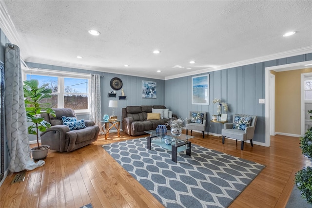 living room featuring a textured ceiling, ornamental molding, visible vents, hardwood / wood-style floors, and baseboards